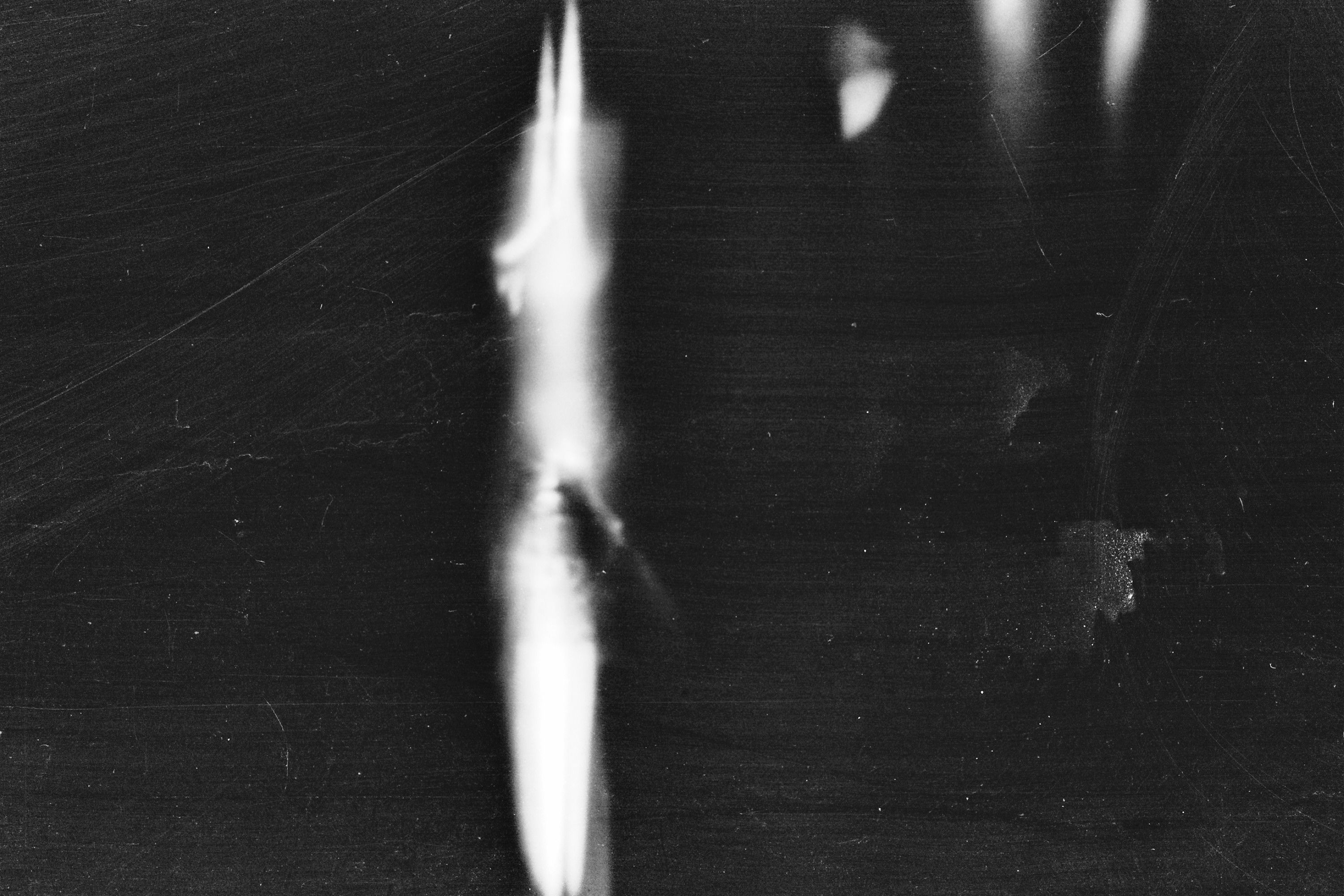 Abstract black-and-white film scan with light leaks and scratches, evoking analog imperfection and unfiltered character.