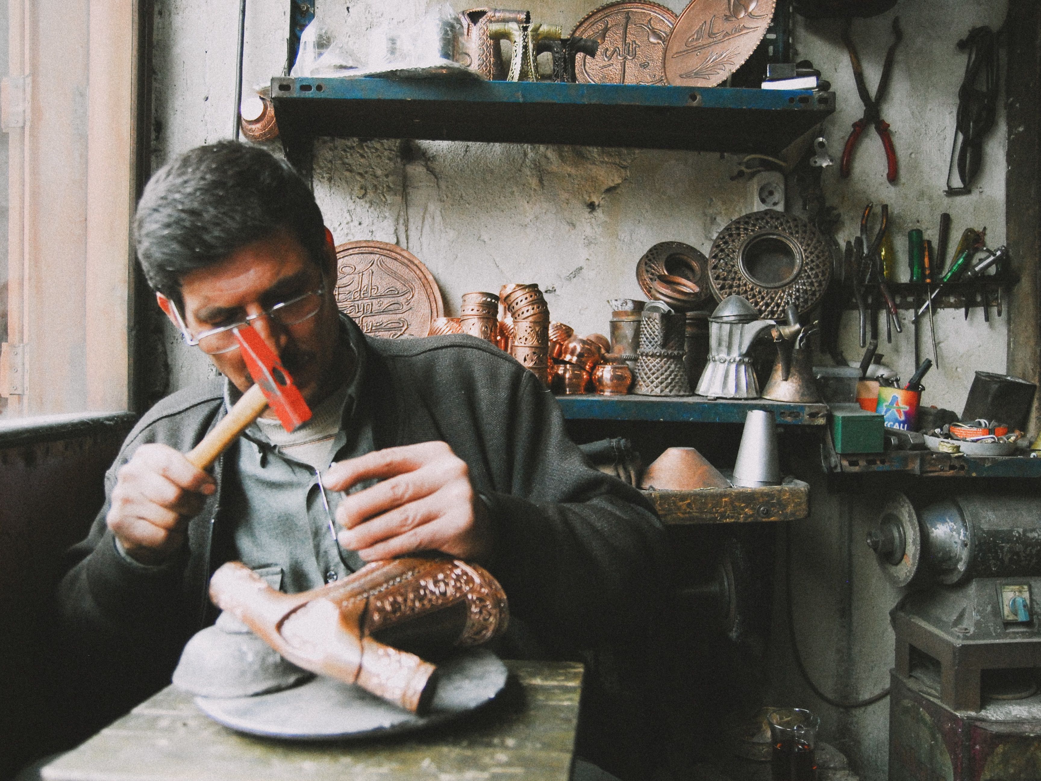 Artisan shaping copperware by hand in a traditional workshop, illustrating visible craftsmanship and individuality.